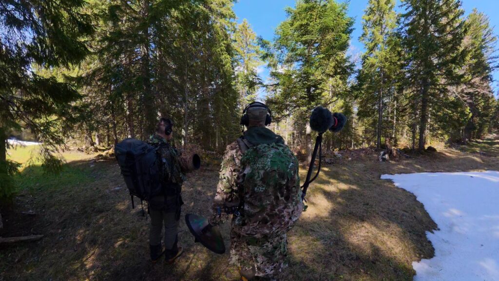 Deux personnes équipées de casques écoutent en forêt avec le rig Hooter et le micro binaural monté sur le sac.
