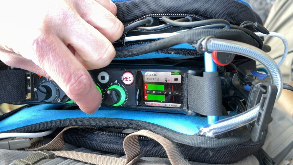 Main sur le Sound Devices MixPre-6 II pendant une prise Hooter, avec les potentiomètres de gain, l'écran de monitoring et les câbles du rig.